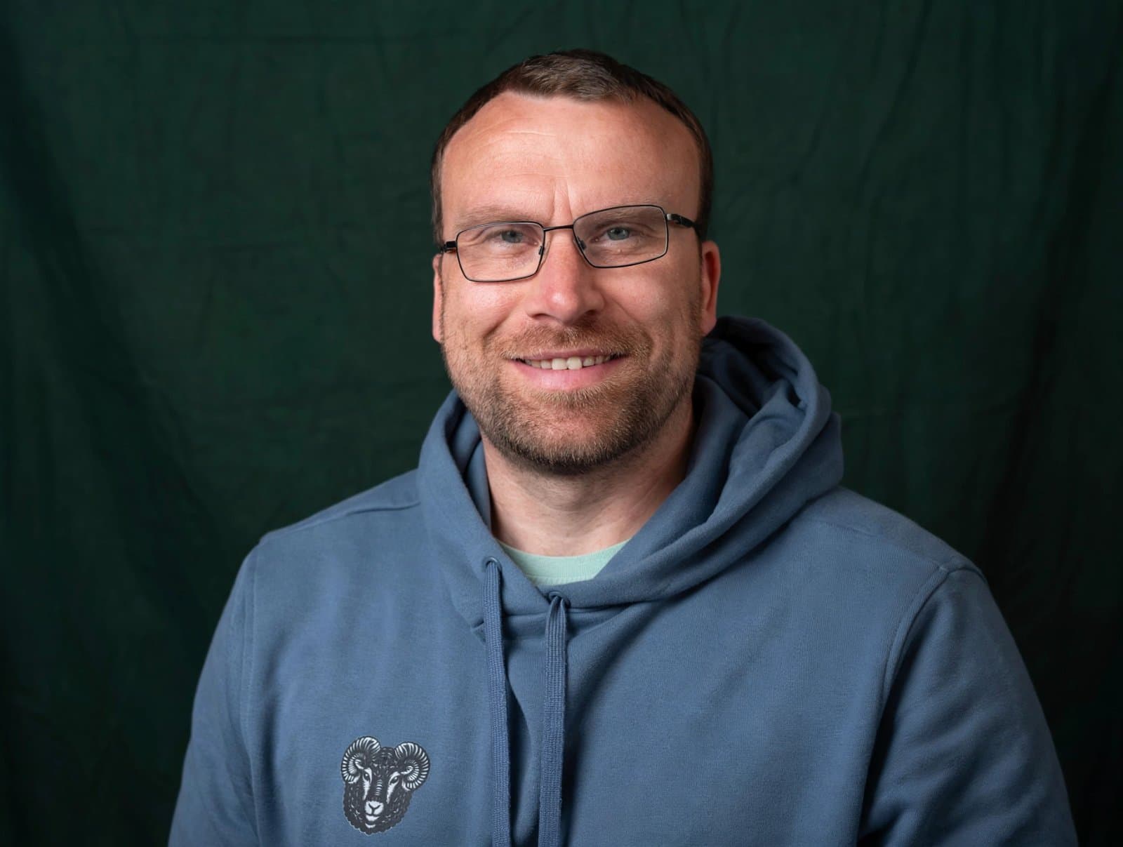 Ken Selfie wearing a blue black sheep wellbeing hoodie in front of a green background.